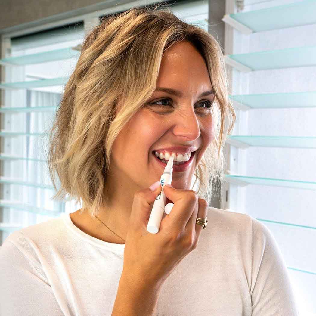 Kvinde smiler, mens hun bruger SmilePro tandblegningspen